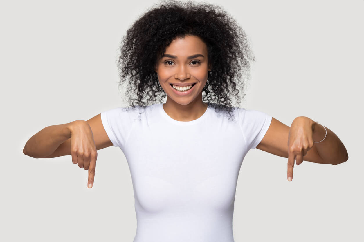 A Woman With Black Hair And Wearing A White Shirt Pointing Down With Both Hands